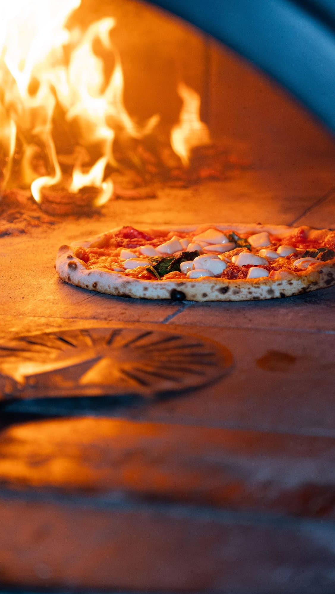 A pizza turning in the flame of the wood-fired oven
