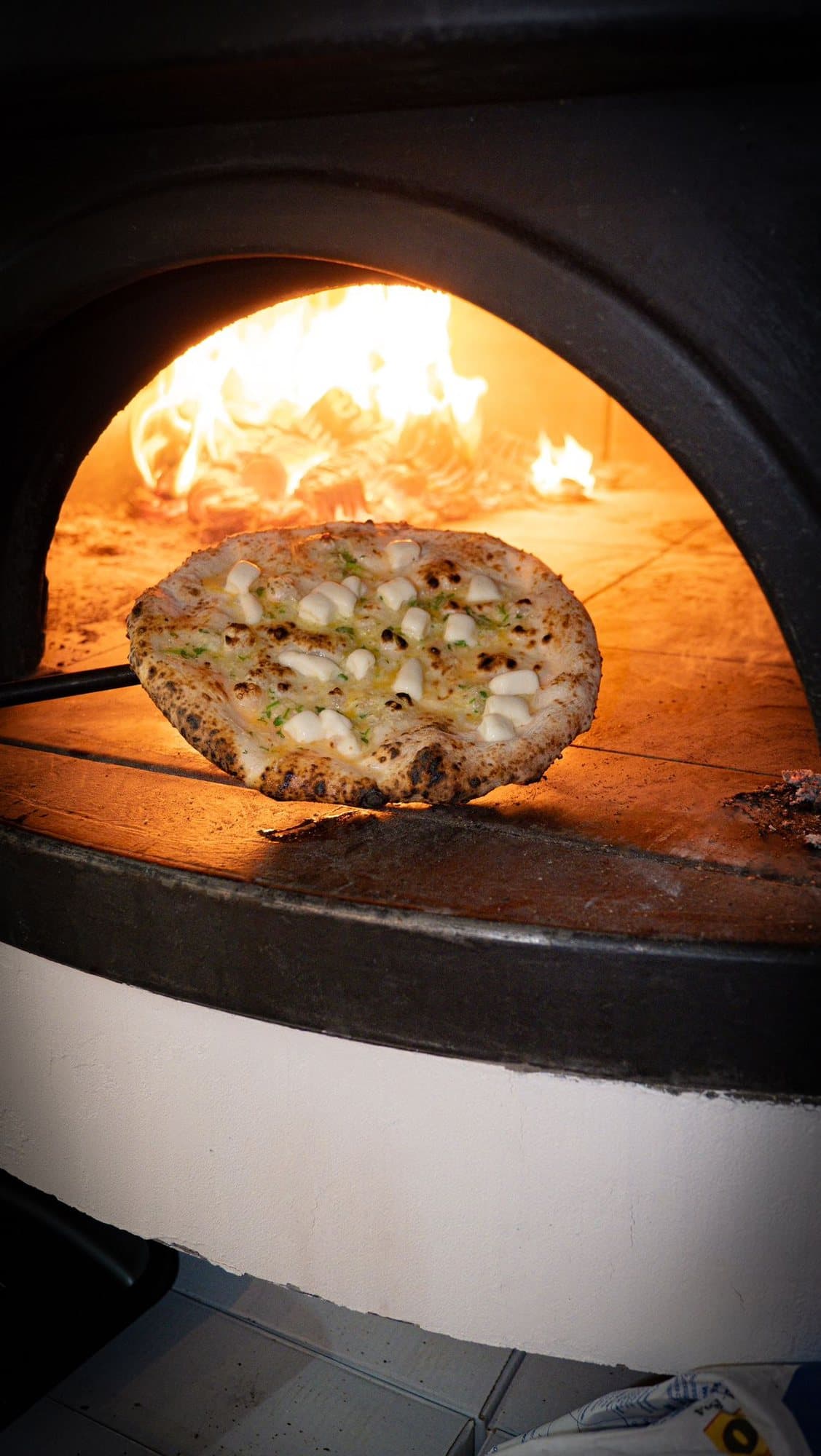 A pizza on the peel against the flame of the wood-fired oven